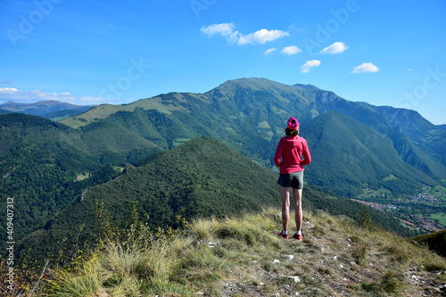 Woman standing on the summit of Corna Trentapassi overlooking Monte Guglielmo and other mountains. Lago d'Iseo, Brescia, Lombardy, Italy.