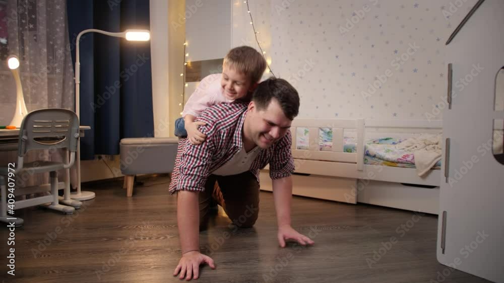 Happy smiling father with little son playing and riding piggy back at bedroom. Concept of child playing with parents and family having time together at night