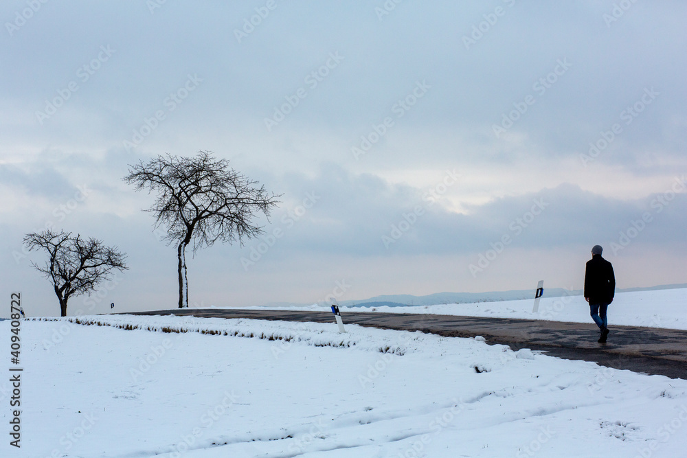Fototapeta premium Lonely figure walking past a tree on a hill in rural place in winter 