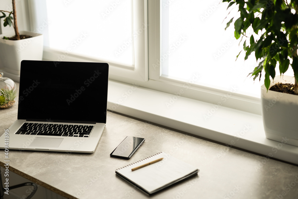 Still life view of office room with open laptop computer on desk with reflections by bright window, office interior. Professional workplace technology indoors. Still life view of office room with open laptop computer on desk with reflections by bright window, office interior. Professional workplace technology indoors.