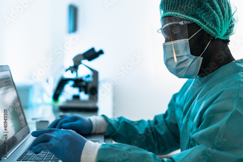 Medical worker wearing personal protective equipment using computer inside clinic during corona virus outbreak - Research and development concept