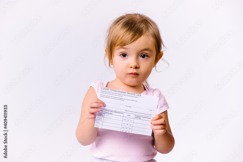 Little girl with a vaccination card looks at the camera on a white background with blank side space. Little girl with a vaccination card looks at the camera on a white background with blank side space.