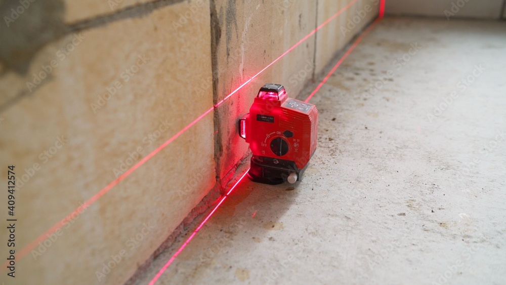 The construction laser level is on the floor. The beam is directed at the wall. Aligning the walls with a laser level. The construction laser level is on the floor. The beam is directed at the wall. Aligning the walls with a laser level.