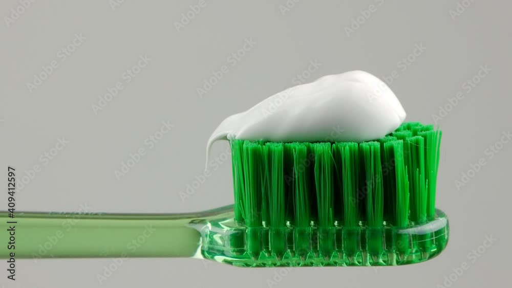 White toothpaste is placed on a green toothbrush on a white background in close-up. White toothpaste is placed on a green toothbrush on a white background in close-up.