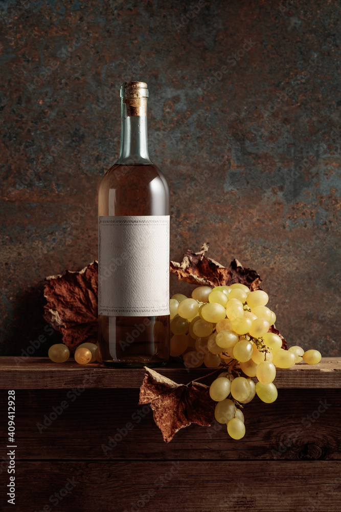 Naklejka premium Bottle of white wine with grapes and dried up vine leaves.