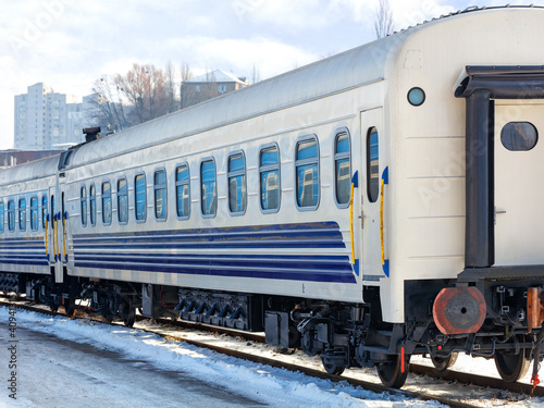 The white railroad car of the train stands on the tracks on a bright winter day.
