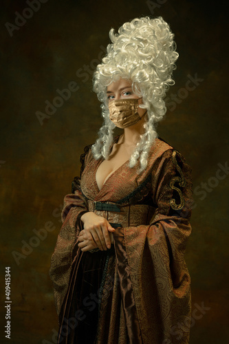 Portrait of medieval young woman in vintage clothes, golden face mask posing confident on dark background. Royal person protected from covid. Concept of comparison of eras, modern, fashion.