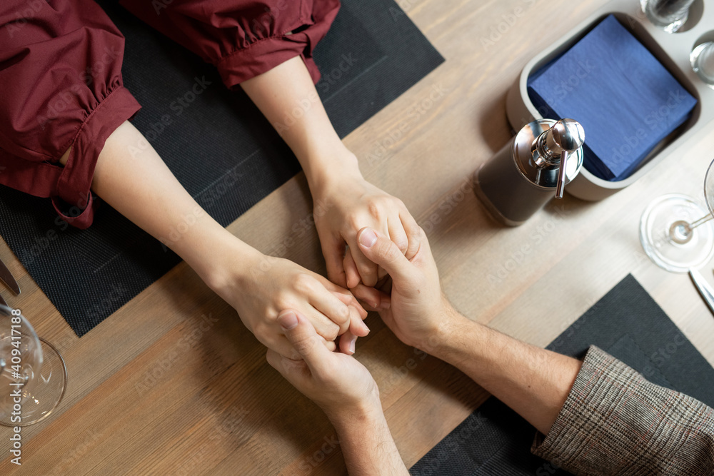 Overview of young affectionate man and woman holding by hands by table