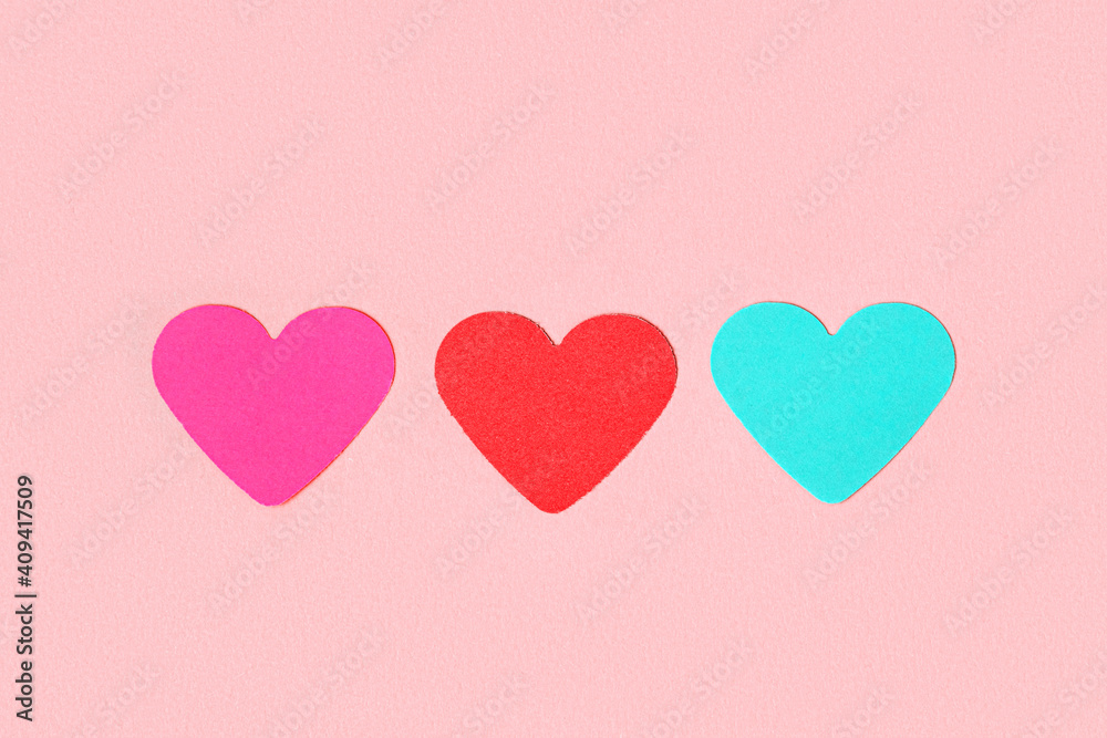 Three multi-colored hearts cut from paper on a pink background. Different love of all colors.