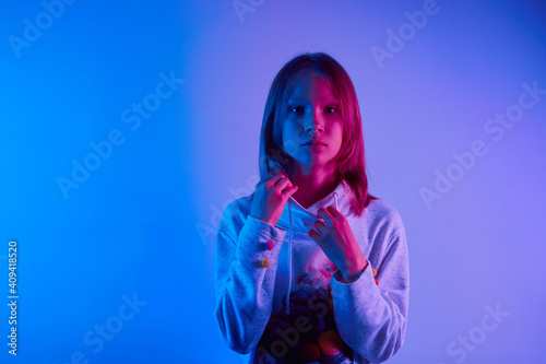 Teen girl standing and posing over trendy blue neon light. Portrait of millennial pretty teenager.