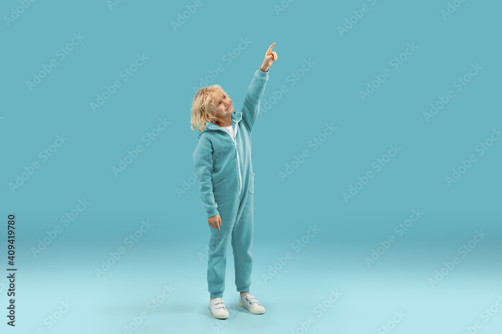 Pointing up. Childhood and dream about big and famous future. Pretty curly boy isolated on blue studio background. Childhood, dreams, imagination, education, facial expression, emotions concept. Pointing up. Childhood and dream about big and famous future. Pretty curly boy isolated on blue studio background. Childhood, dreams, imagination, education, facial expression, emotions concept.