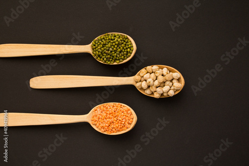 Top view on red lentils, chickpea and mash in the wooden spoons on the dark background