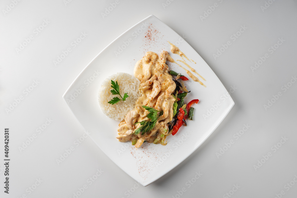 Slices of chicken breast fillet in cream sauce with rice and vegetables, top view Slices of chicken breast fillet in cream sauce with rice and vegetables, top view