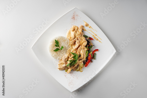 Slices of chicken breast fillet in cream sauce with rice and vegetables, top view