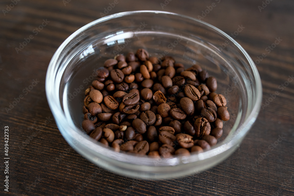 Glass bowl with roasted coffee beans on wooden table prepared for grinding Glass bowl with roasted coffee beans on wooden table prepared for grinding