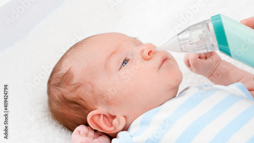 Closeup of mother using electric nasal aspirator to remove mucus from her newborn baby nose. Concept of babies and newborn hygiene and healthcare. Caring parents with little children. photo