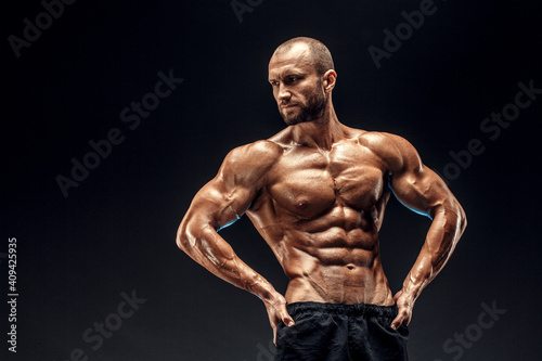 Strong man with perfect abs, shoulders, biceps, triceps and chest. Bodybuilder topless flexing his muscles over black background.