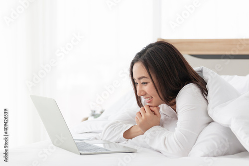 Young female lying on bed using notebook computer. Happy female using laptop at home in bedroom. Working from home in quarantine lockdown. Women watching movie on laptop lying in bed.
