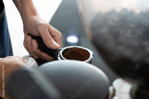 Closeup of Barista hand holding ground coffee for preparing espresso. Barista preparing portafilter before making cappuccino in a coffee shop. Barista holding portafilter tamping.