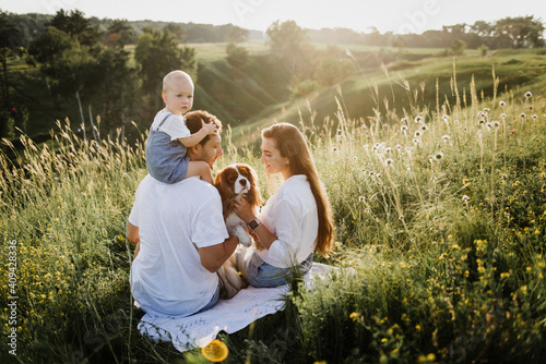 Young beautiful family with a little daughter and a dog hug, kiss and walk in nature at sunset.