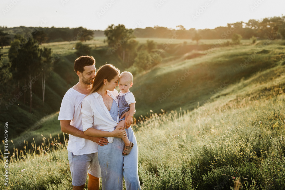 Young beautiful family with a little daughter hug, kiss and walk in nature at sunset. Photo of a family with a small child in nature. Young beautiful family with a little daughter hug, kiss and walk in nature at sunset. Photo of a family with a small child in nature.