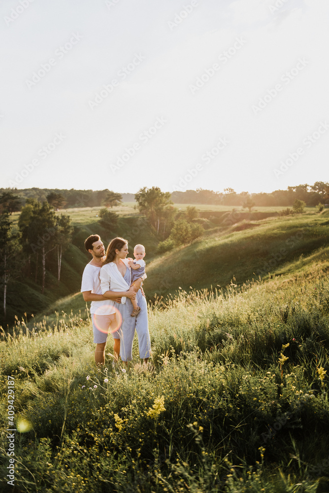 Young beautiful family with a little daughter hug, kiss and walk in nature at sunset. Photo of a family with a small child in nature.