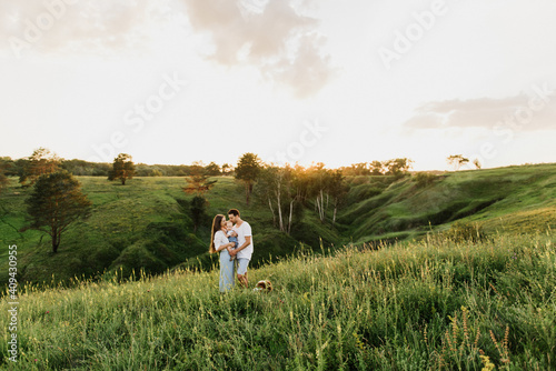 Young beautiful family with a little daughter and a dog hug, kiss and walk in nature at sunset. © Oksana