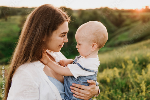 Young beautiful mother with her little daughter hug, kiss, laugh and walk in nature at sunset. Photo of a mother with a small child at sunset.