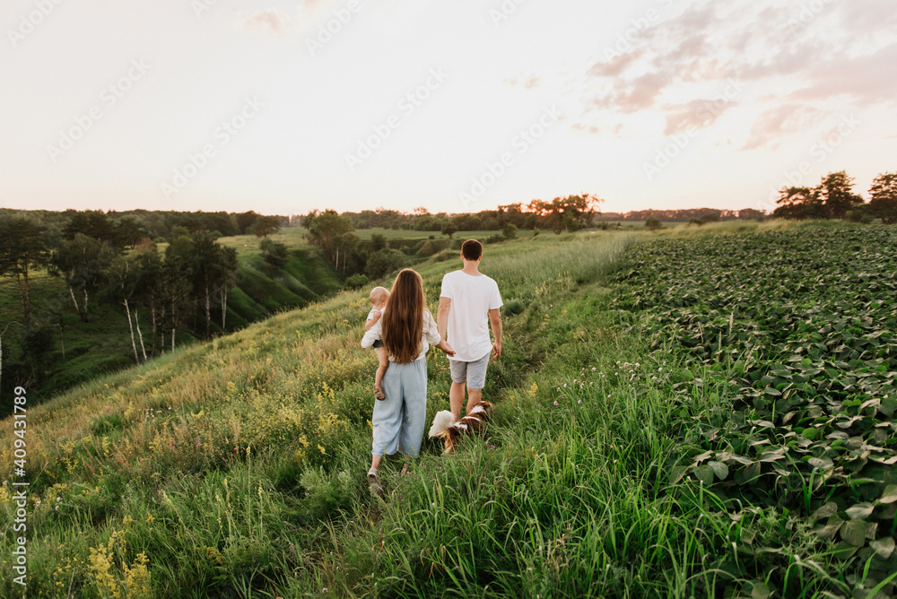 Young beautiful family with a little daughter and a dog hug, kiss and walk in nature at sunset. Young beautiful family with a little daughter and a dog hug, kiss and walk in nature at sunset.