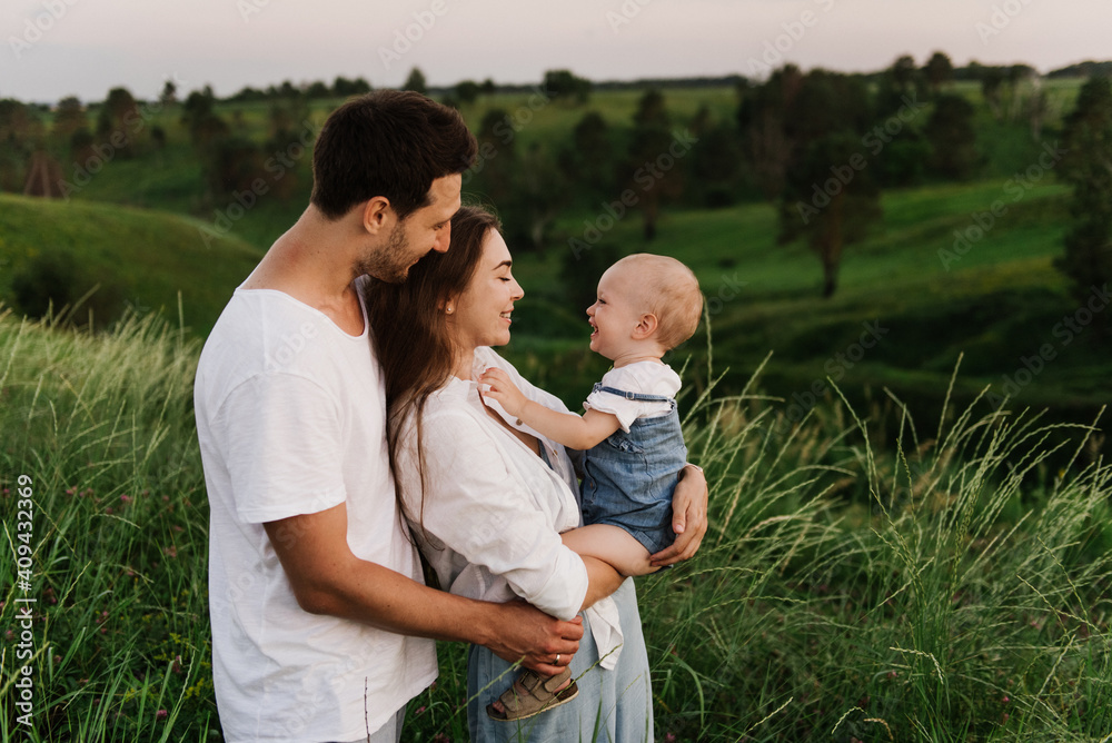 Young beautiful family with a little daughter hug, kiss and walk in nature. Photo of a family with a small child in nature. Young beautiful family with a little daughter hug, kiss and walk in nature. Photo of a family with a small child in nature.