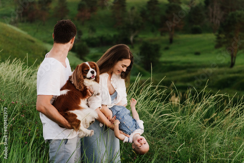 A young beautiful family with a little daughter and a dog hug, kiss and walk in nature. Photo of a family with a small child in nature.