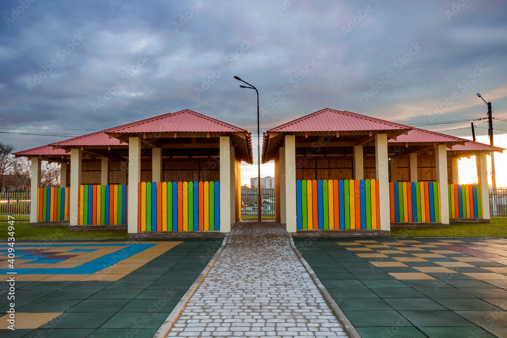 Kindergarten playground with bright new alcove with multicolored low fence, big yard with soft rubber flooring on blue sky copy space background. Perfect place for children activities outdoors.