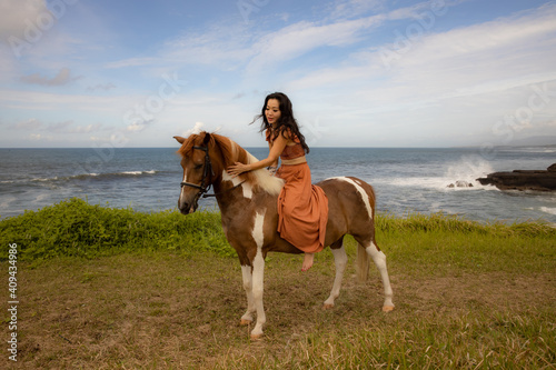 Asian woman riding horse near the ocean. Outdoor activities. Wcuddling her horse. Traveling concept. Copy space. Bali