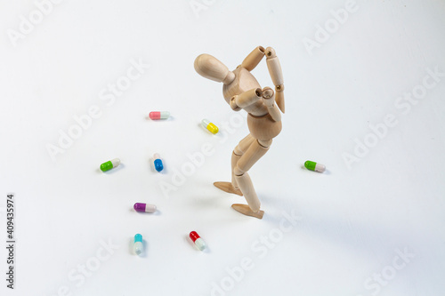 a bent wooden mannequin with back pain among colorful pills on white background