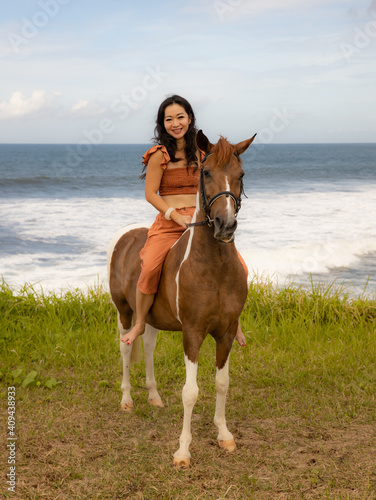 Happy smiling woman riding horse near the ocean. Outdoor activities. Human and animals relationship. Traveling concept. Copy space. Bali