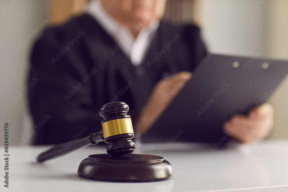 Close up of a dark brown judge's gavel on the table against the background of a judge reading the verdict. Concept of justice, law, jurisprudence and court proceedings. Blurred background.