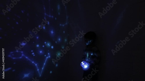 Little Asian boy in his room with night light projecting stars on room ceiling. Children read before bedtime.