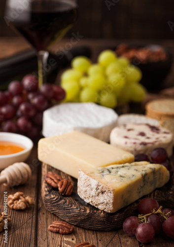 Glass of red wine with selection of various cheese and grapes on wooden background. Blue Stilton, Red Leicester and Brie Cheese and bowl of nuts and crackers. Top view