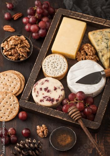 Selection of various cheese in vintage box grapes on wooden table background. Blue Stilton, Red Leicester and Brie Cheese and nuts with crackers and honey.