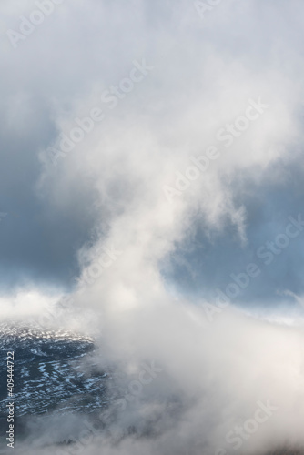 Epic landscape image of Skiddaw snow capped mountain range in Lake District in Winter with low level cloud around peaks viewed from Derwentwater