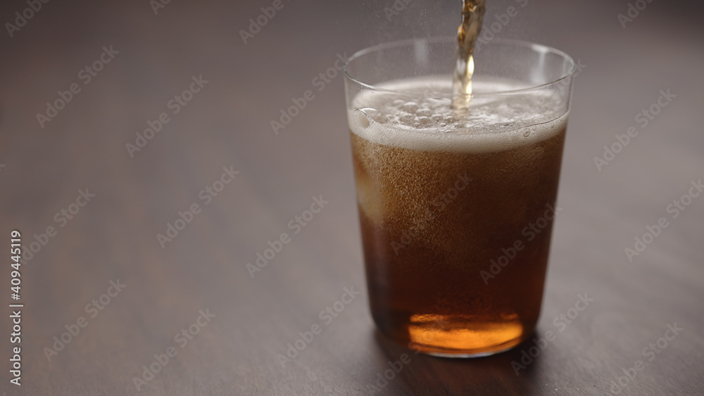 pour cola over ice cubes into tumbler glass on walnut table with copy space pour cola over ice cubes into tumbler glass on walnut table with copy space