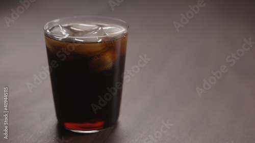 pour cola over ice cubes into tumbler glass on walnut table with copy space