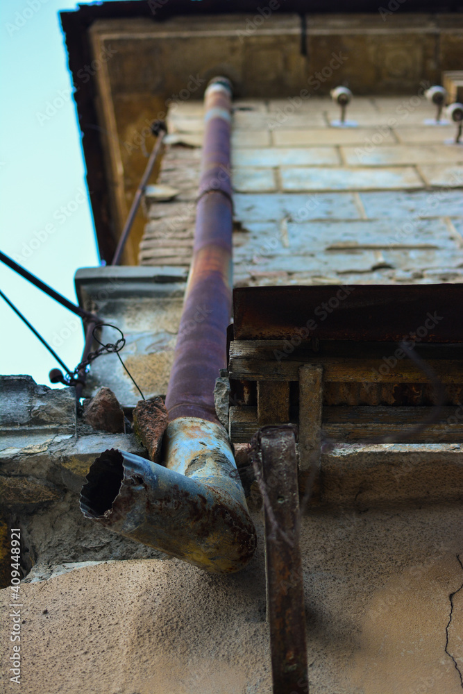 Closeup of a rusted old vintage roof rain gutter pipe, on old damaged house.