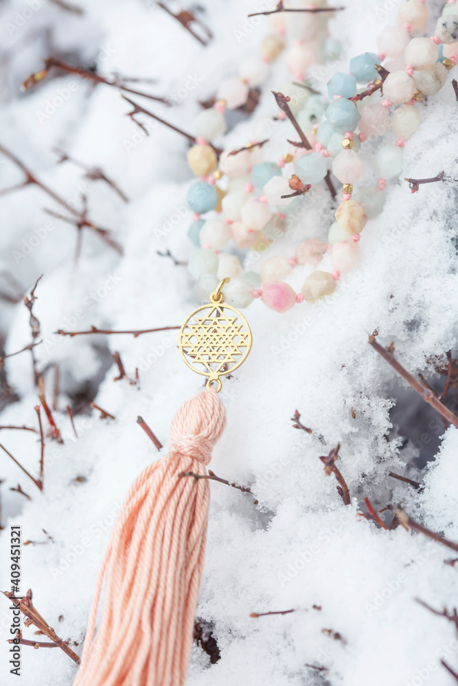 Naklejka premium Brass metal spiritual symbol of yantra faceted morganite mala necklace on the white snow