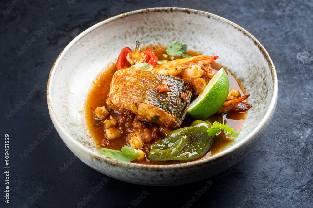 Modern style traditional Mexican seafood pozole soup with fish, king prawns and hominy in a clear sauce served as close-up in design bowl Modern style traditional Mexican seafood pozole soup with fish, king prawns and hominy in a clear sauce served as close-up in design bowl