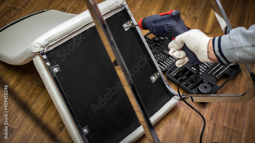 Drilling a hole in furniture, male homeworker repairing furniture with tools photo
