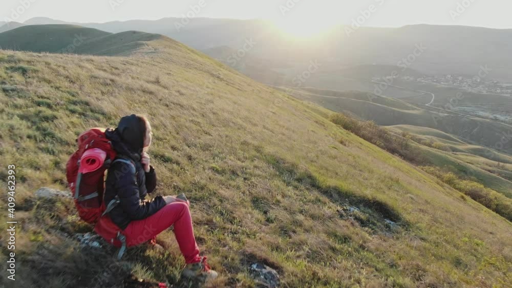 A couple of young tourists sit on the rocks on the hillside and watch the sunset. Joint active rest of a young couple. A couple of young tourists sit on the rocks on the hillside and watch the sunset. Joint active rest of a young couple.