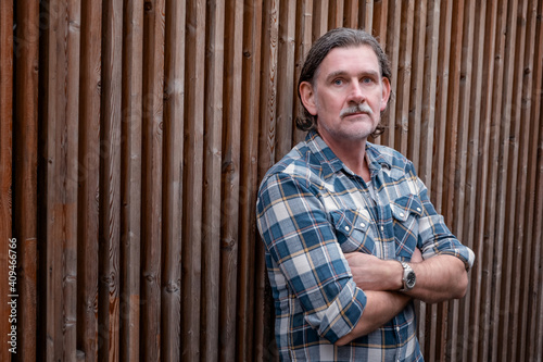 portrait of a handsome man in his 50s standing by wooden fence