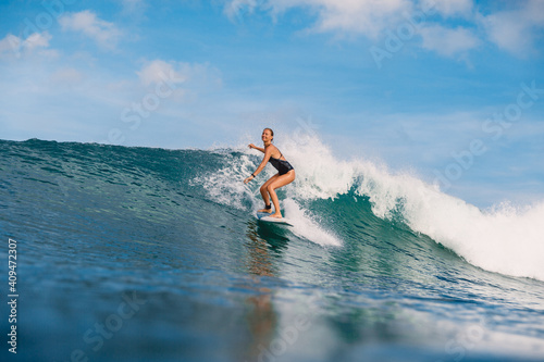 Surfer woman at surfboard on blue wave. Sporty woman in ocean during surfing.