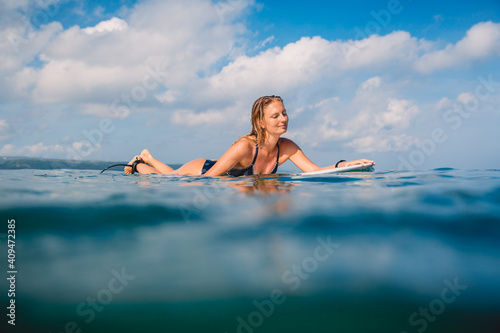 Attractive surfing woman with surfboard. Surfgirl paddle on surfboard in ocean
